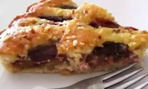 Una fetta di torta con prugne fresche, con crosta dorata e ripieno succoso, pronta per essere gustata.