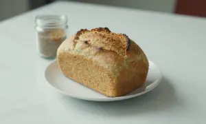 Chleb z mąki ryżowej, lekko przypieczony, na białym talerzyku. Obok słoiczek z ziarnami.