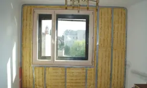 Izolacja akustyczna wokół okna, z widocznym materiałem w kolorze piaskowym na ścianie, przygotowana do dalszych prac wykończeniowych.