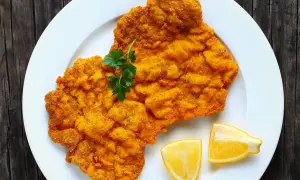 Ein knuspriges Wiener Schnitzel auf weißem Teller, garniert mit Petersilie und Zitronenspalten. Perfekt für einen herzhaften Genuss.