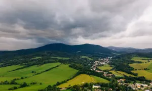 Malownicze **góry stołowe**, gdzie można znaleźć urokliwy **nocleg**. Zielone pola i lasy otaczają niewielką wioskę, a nad wszystkim górują ciemne chmury.