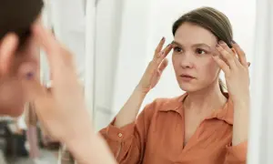 Kobieta w lustrze, dotykając twarzy, zamyślona. Czy to, co widzi, odzwierciedla jej prawdziwe ja, czy to tylko zaburzony obraz siebie?