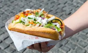 Kebab w picie z warzywami i serem feta, trzymany w dłoni.