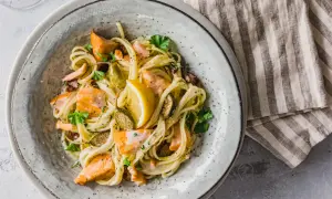 Ein Teller mit cremigen Nudeln mit Lachs, garniert mit Zitrone und Petersilie.