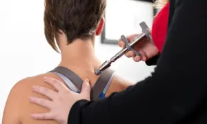 Thérapeute utilisant un appareil pour soulager la douleur haut du dos gauche d'une patiente.