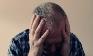 Mężczyzna w kratę trzyma się za głowę, jego twarz ukryta w dłoniach. Widać oznaki dekompensacji i przytłoczenia.