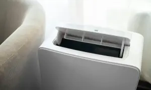 Nowoczesny klimatyzator bez jednostki zewnętrznej, z otwartą klapą wentylacyjną, obok jasnej kanapy.