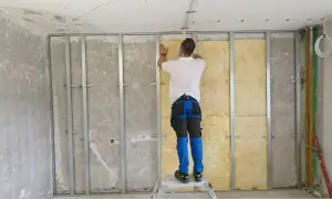 Pracownik montuje wełnę mineralną, by zapewnić wyciszenie sufitu od sąsiada. Metalowy stelaż i izolacja to klucz do ciszy.