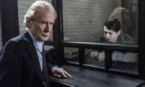 En äldre man i kostym tittar mot en yngre man bakom galler. Scen från huset på udden serie.