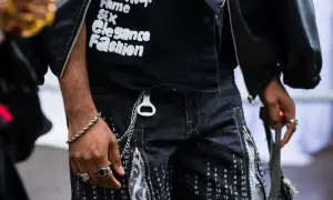 Mężczyzna w czarnej kurtce i spodniach z nadrukiem cyfrowym, z biżuterią i brelokiem w kształcie otwieracza. Styl opium.