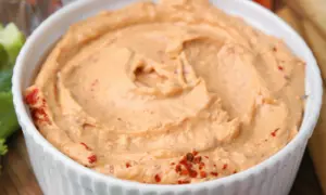 Kremowe smarowidło z suszonych pomidorów w białej miseczce, ozdobione płatkami chili.