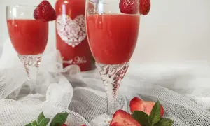 Dwa kieliszki z orzeźwiającym, czerwonym drinkiem, ozdobione truskawkami. Obok butelka z napisem "Sweet Heart", sugerująca pyszny alkohol truskawkowy.