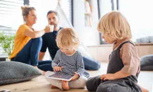 Rozpieszczone dziecko pochłonięte tabletem, podczas gdy rodzice w tle piją kawę.