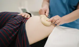 Une main ajuste un moniteur sur le ventre d'une femme enceinte. Apprendre à comment lire un monitoring est essentiel pour le suivi de grossesse.