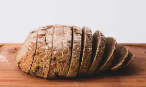 Pokrojony bochenek ciemnego chleba z ziarnami na drewnianej desce.