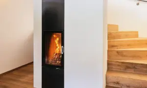 Ein moderner Kamin mit brennendem Feuer, daneben eine Holztreppe. Hier sieht man, was ein Grundofen leisten kann: Wärme und Gemütlichkeit.