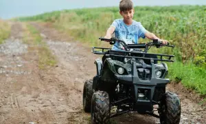 Chłopiec na quadzie, kategoria B1, jedzie po błotnistej drodze wśród zielonych pól.