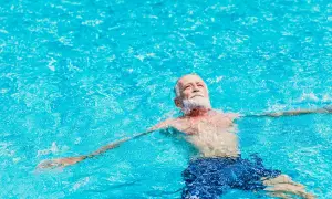 Ein älterer Mann mit Bart entspannt sich im Wasser. Schwimmen bei Arthrose kann Linderung verschaffen.