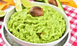Miseczka guacamole z pestką, limonką i nachos w tle na czerwono-białej kratce.