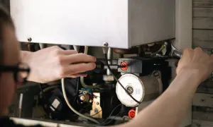 Un technicien ajuste le pilotage du chauffe eau avec un tournevis et une clé.