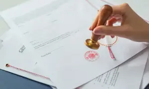 Dłoń z pieczęcią notarialną wykonuje własnoręczne poświadczenie za zgodność z oryginałem na dokumentach.