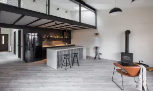 Nowoczesna kuchnia z wyspą i antresolą. Inspiracje dla loftowych wnętrz, gdzie industrialny styl łączy się z przytulnością kominka i wygodnym fotelem.