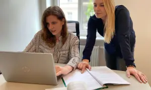 Dwie kobiety pracują nad dokumentami i laptopem, przygotowując wniosek o rozwód online.