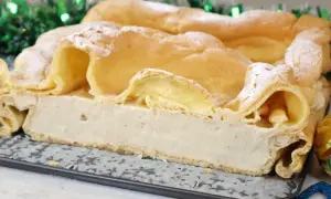 Puszyste ciasto karpatka z kremem waniliowym, udekorowane cukrem pudrem, na tle świątecznych lampek.