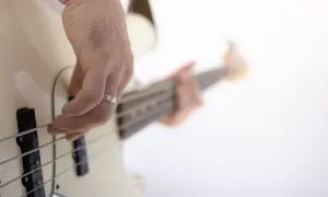 Dłoń z obrączką gra na białej gitarze basowej.