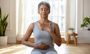 Femme pratiquant une technique de relaxation mentale, mains sur la poitrine et le ventre, yeux fermés, dans une pièce lumineuse.