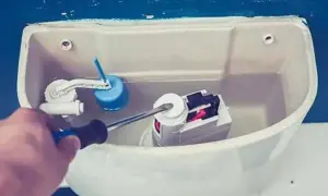 Mano con cacciavite che regola il meccanismo interno di uno scarico del water.
