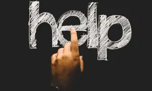 Palec wskazuje literę "e" w napisie "help" na tablicy. To symboliczne wezwanie o pomoc, często pojawiające się w kontekście psychologii rozwojowej.