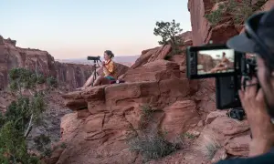 Krystle Wright, fotografa, siede su una roccia rossa in un canyon, mentre un operatore riprende la scena.