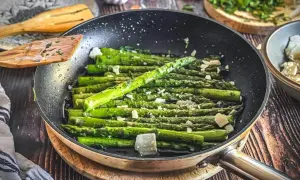 Grüner Spargel wird in einer Pfanne mit Käse und Kräutern zubereitet. Ein köstliches Gericht, das zu vielen Spargel Rezepten passt.