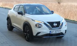 Biały Nissan Juke Sport z czarnym dachem i felgami, zaparkowany na kostce brukowej przy suchej trawie.
