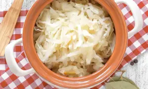 Sauerkraut in einem Tontopf mit kariertem Tuch, Lorbeerblättern und Pfefferkörnern.