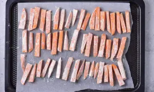 Pokrojone frytki z batatów posypane mąką na blasze do pieczenia.