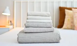 Neatly folded stack of clean bed sheets on a white bed, ready for how to wash bed sheets in washing machine.