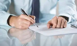 Mężczyzna podpisuje dokument, być może prolongata umowy. Dłoń z piórem nad papierem.