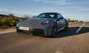 Szary Porsche 911 GTS sunie po krętej drodze, otoczony jesiennym krajobrazem.