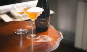 Dwa kieliszki koktajlowe z kolorowymi kropkami i butelka kombuchy na drewnianym stole. Czy kombucha ma alkohol? Ta butelka sugeruje, że może mieć.