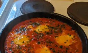 En varm och bubblande shakshuka med ägg i tomatsås, perfekt för ett mysigt frukostrecept.