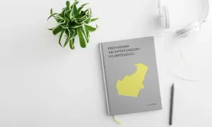 Przewodnik architektoniczny po Wrzeszczu, słuchawki i długopis na białym tle. Zielona roślina w doniczce.