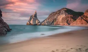 Piękny zachód słońca na plaży Praia da Ursa, z mglistymi falami i skalistymi formacjami.