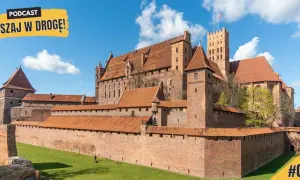 Potężny zamek w Malborku, z czerwonej cegły, z licznymi wieżami i murami obronnymi, na tle błękitnego nieba z chmurami.