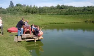 Dzieci i dorośli łowią ryby na drewnianym pomoście. Malownicze łowisko pod lasem Bielany Wrocławskie.