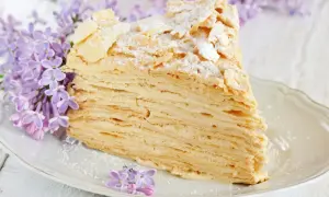 Pyszny tort napoleon z delikatnym kremem i chrupiącymi warstwami ciasta, ozdobiony płatkami migdałów i cukrem pudrem, w otoczeniu kwitnącego bzu.