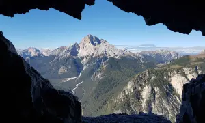 Blick aus einer Höhle auf die majestätische Monte Piana, umgeben von weiteren Gipfeln und grünen Tälern.
