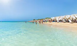 Spiaggia affollata in Puglia, con gente che fa il bagno nelle acque cristalline e si rilassa sotto i gazebo bianchi.