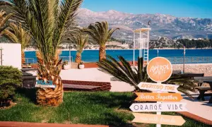 Palmy, morze i góry w Czarnogórze. Znaki wskazują plażę, Aperol Spritz i "Orange Vibe". Idealne miejsce na wakacje.